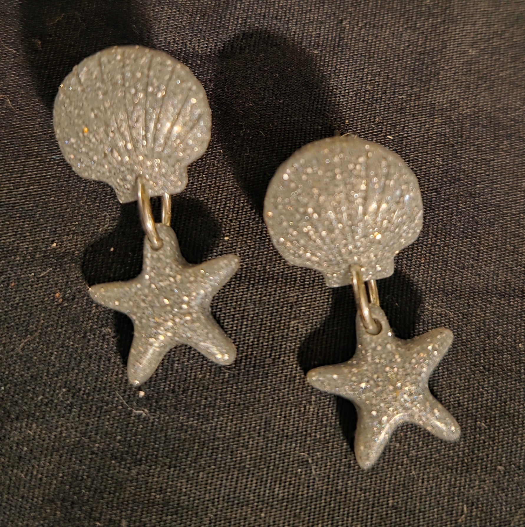 Pair of silver earrings with shell and starfish designs on a dark background